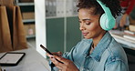 Woman, phone and headphones for logistics at startup with reading, typing and listen to music. Person, smartphone and streaming in warehouse for shipping, mobile app or distribution for supply chain