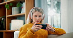 Woman, phone and ebook with headphones for sound, audio book or streaming on living room couch at home. Young female person in relax with headset and reading on mobile smartphone for online learning