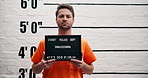 Man, criminal and law with sign for mugshot, violation or investigation of arrest in prison. Portrait of young male person or thief with orange clothing, billboard or number for jail photo or picture