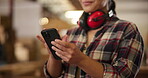 Woman, phone and woodwork with headphones in workshop for safety, noise cancelling and research furniture design. Smile, female carpenter and mobile for project, communication and production factory