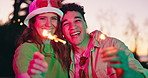 Couple, outdoor and face with sparkles for celebration, festival and party at sunset together. Happy, smile portrait and night event with firework, light and glow at park with love, bonding and care