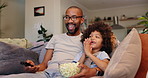 Happy dad, child and watching tv with popcorn for movie, entertainment or bonding on sofa at home. Father, kid or young little boy with remote for online streaming or cartoon in living room at house