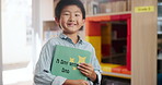 Boy, child and face with book in kindergarten, happiness for storytelling or literacy education. Male student, youth classroom and kid with smile for knowledge or learning, excited for language