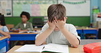 Education, exam and stress with boy student at desk in classroom for development. learning or study. Book, headache and scholarship with child reading at school for academy evaluation or knowledge