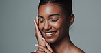 Skincare, face and beauty of happy Indian woman in studio isolated on gray background. Touch, smile and young model in makeup for facial cosmetics, dermatology or healthy glow with eyes closed at spa