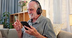 Senior man, sofa and dancing on smartphone with headphone for music playlist and smile for entertainment. Nostalgic, lounge and couch on internet for streaming platform with song or album and video