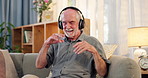 Senior, happy man and dancing with headphones on sofa for music, radio or podcast in relax at home. Elderly or male person with smile or headset for sound or audio therapy in living room at house