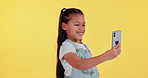 Selfie, happy and child in studio smile for social media, online post and profile picture. Youth, childhood and young girl take photo with funny filter, mobile app and recording on yellow background