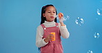 Fun, blow and child in studio with bubbles for magic, playing and games for growth, development or celebration. Girl, soap and liquid solution for playful entertainment, curiosity and blue background