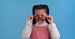 Fashion, sunglasses and face of child in studio for confidence, trendy style and cool accessories. Happy, smile and portrait of young girl with eyewear for joy, pride and cute on blue background