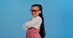 Attitude, sunglasses and face of child in studio for confidence, trendy style and cool accessories. Happy, smile and portrait of young girl with eyewear for fashion, pride and cute on blue background