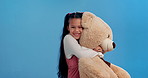 Happy girl, hug and love with teddy bear for toy, friend or joy in studio on a blue background. Portrait of cute child or kid with smile or soft stuffy animal for embrace, happiness or childhood