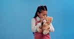 Little girl, whisper and secret with teddy bear for gossip, trust or imaginary friend in studio on a blue background. Sneaky child or young kid talking to soft stuffy animal for confidential rumor