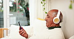 Home, relax and old man with headphones, cellphone and break with radio, listening to music and social media. Pensioner, apartment and senior person on sofa, headset and smartphone with audio or song