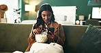 Popcorn, phone and woman relaxing on sofa watching funny video on social media or internet. Cellphone, smile and female person eating snack and reading comic blog on website in bedroom at apartment.