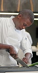 Black man, chef and cutting green onion fast in kitchen for food, dinner and healthy lunch. Knife, cooking and professional with scallions on chopping board or vegetables for meal prep in restaurant