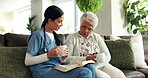 Sofa, senior woman and caregiver with book for reading, listening and discussion with tea cup at home. Couch, elderly person and female nurse for bible session, guidance and wisdom in retirement