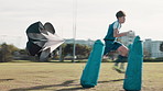 Soccer field, exercise and kid with running parachute at practice for workout, challenge or routine. Sport, team and boy with equipment on grass for resistance, training or development in speed skill