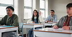 Education, question and student at desk of classroom in school for development, learning or study. Asking, growth or smile with teen people friends in class for academy, lecture or scholarship