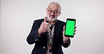 Senior man, thumbs up or phone for green screen, mockup space or app notification in studio on white background. Online ads, face or pensioner on mobile technology for review, announcement or promo