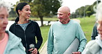 Fitness, instructor and senior group walking with mat at park for workout, exercise or outdoor training in nature. Personal trainer talking to people for stroll, elderly care or health and wellness