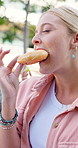 Woman, eating and donut outdoor on campus for picnic, diet and happy for nutrition at college. University student, sweets and dessert in park or garden with gen z people on lawn for lunch break