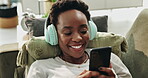 Black woman, relax and phone with headphones on sofa for streaming music, listening audio and dancing at house. Happy, female person and mobile for social media, online video and subscription service