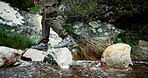 Feet, person and rocks for hiking outdoor with water path, travel journey and trekking adventure of fitness. Hiker, legs and walking on stone for mountain trail, balance exercise and nature workout