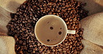 Coffee, above and cup with beans at cafe for strong caffeine, latte or cappuccino on table. Top view or closeup of mug, brew or liquid with brown froth for mocha, espresso or breakfast beverage