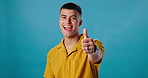 Thumbs up, agreement and portrait of man in studio with positive attitude, like and happy vote. Thank you, smile and person with yes hand gesture for success, emoji and achievement on blue background