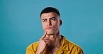 Man, thinking or ponder with question in deep thought for choice or decision on a blue studio background. Young male person or model in wonder or doubt for idea, solution or selection on mockup space