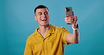 Man, phone and selfie photography in studio, live streaming and check style or fashion on blue background. Male person, app and capture photo for profile picture, social media update and laughing