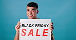 Black Friday, sale and face of man on blue background for promotion, information and sign. Happy, advertising and portrait of person with banner and poster for retail sale, deal and bargain in studio