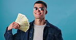 Face, winner and man with cash, finance and confident person on blue studio background. Portrait, happy guy and model with prize money, bonus and savings with investment, profit and salary increase