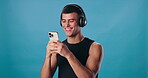 Man, cellphone and texting in studio with fitness, headphones and smile for workout. Happy athlete, mockup and technology with laugh, exercise and streaming podcast or music on blue background