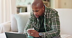 Black man, home and laptop with coffee on sofa with research for house finance or loan application. Male person, couch and living room on website or internet on comparing for mortgage interest rate 