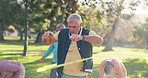 Senior man, hula hoop and park with group for exercise class, fun workout or elderly care in fitness. Happy, mature male person or people with toy for movement, balance or stretching muscle in nature