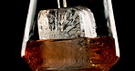 Glass, ice and pour drink in studio for enjoyment, refreshing and cold beverage. Frozen cube, tumbler and whiskey flow on black background with liquor, brandy and aesthetic for testing in distillery