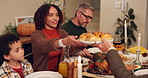 Food, happy family and eating dinner for thanksgiving celebration or gratitude in home at night. Child, mom and dad share meal in plate or serving bread buns and interracial people bonding together