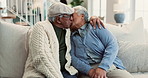 Senior, couple and kiss on sofa with love for marriage, commitment and romance in retirement. Elderly, people and embrace in home with laughing, happy and talking in living room for bonding or relax