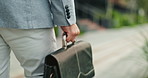 Hands, briefcase and business person in city with travel, walking and morning commute as lawyer career. Attorney, storage bag and professional for legal case, sidewalk and justice of urban path