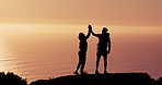 Couple, mountain and hiking with high five at sunset with ocean, success and silhouette on vacation in summer. Goals, partner and person with disability, achievement and prosthetic leg with sea view