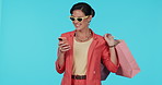 Mobile app, shopping bag or happy woman on social media for online fashion in studio on blue background. Phone, smile or rich girl with news notification on discount deal or promotional sale offer