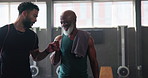 Mature man, personal trainer and fist bump in gym for exercise, workout or training. Physical therapy, support and help with routine with fitness, equipment and wellness for retirement health