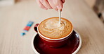 Person, stir and hand with coffee on table for morning, sweetener and preparation of beverage. Mixing, sugar and top view with mug by customer for restaurant, cappuccino and caffeine in warm drink