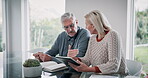 Book, tablet and senior couple with discussion at table for insurance payment, financial bills or loan. Elderly people, retirement and talking with tech at home for pension, healthcare debt or budget