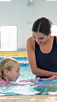 Teacher, woman and girl in swimming pool for learning with smile, support and helping hand to float. Person, coach and child in water with practice for balance, stroke and development with safety