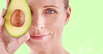 Avocado, beauty and eye of mature woman closeup on green screen for cosmetic skincare treatment. Food, portrait and wellness with wrinkles of person in studio for collagen, dermatology or detox