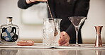 Hospitality, person and bartender stirring ice in glass for catering, service and mixology technique. Professional, server and hands preparing alcohol with utensil for restaurant, event and beverage