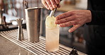 Hands, tongs and bartender with lemon in cocktail for drink preparation closeup in pub. Alcohol, glass or barman with fruit slice on ice to garnish liquor on rocks for decoration, art or presentation